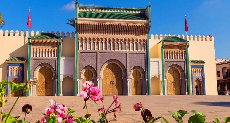 Ornate mosaic royal gateway with green tiled roofs framed by blooming flowers
