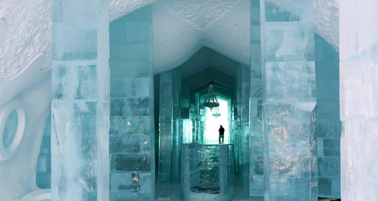 Un visiteur se tient au bout d'un couloir glacé bordé de piliers de glace bleu translucide dans le célèbre Hôtel de Glace.