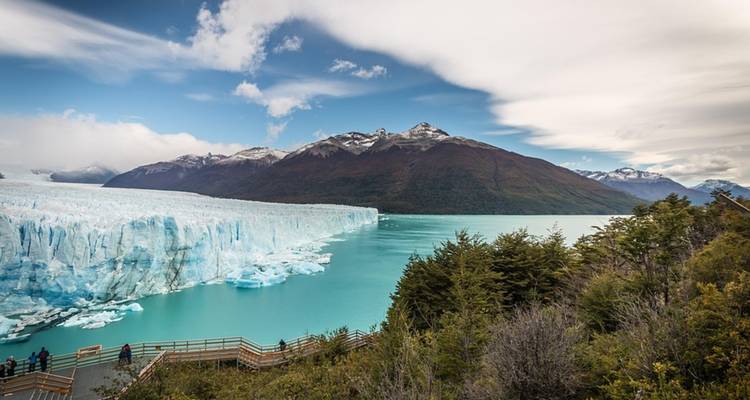 Een weids panorama van het turkooizen glaciërmeer omgeven door Perito Moreno's ijsmuur en sneeuwbedekte bergtoppen, gezien vanaf houten loopbruggen.