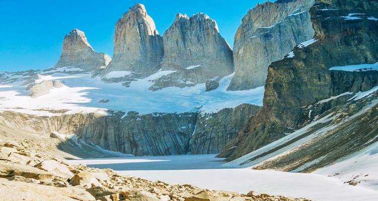 De met sneeuw bestoven granieten torens van Torres del Paine torenen boven een bevroren meer uit onder heldere blauwe luchten.