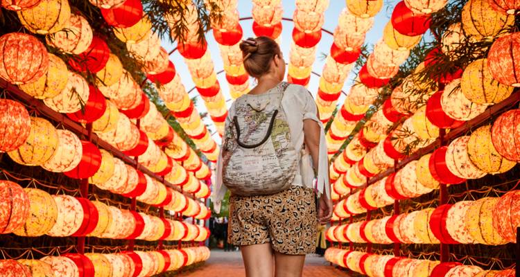 Une voyageuse marche dans un tunnel de lanternes rouges et jaunes brillantes à Hoi An.
