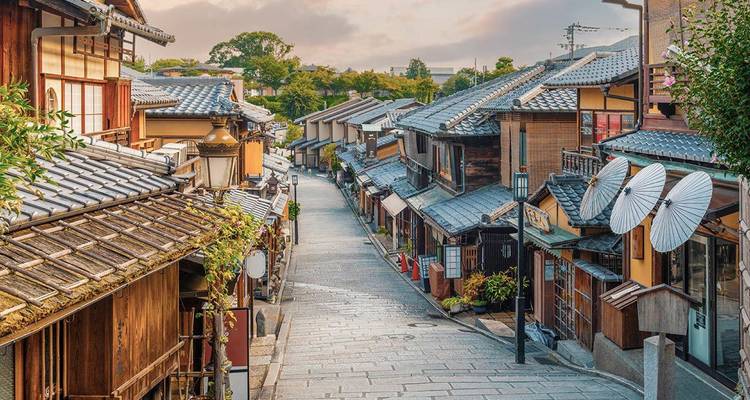 Een tijdloze stenen steeg omzoomd met traditionele houten machiya-huizen en papieren parasols in Kyoto's Higashiyama-wijk bij het aanbreken van de dag.