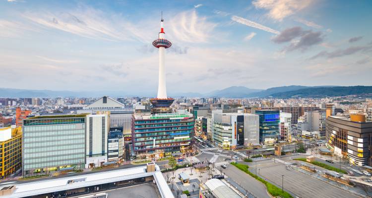 Panoramisch stadslandschap van Kyoto met de wit-rode Kyoto Tower die bij zonsondergang boven moderne gebouwen uittorent.