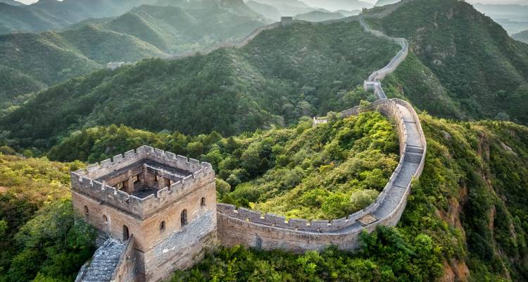 Die Chinesische Mauer schlängelt sich über üppig grüne Bergkämme unter sanftem Morgenlicht und nebligen fernen Gipfeln.