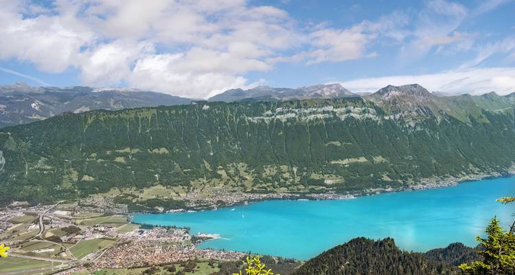 Amplio panorama aéreo de un lago alpino de un turquesa brillante rodeado de montañas verdes empinadas y pueblos.