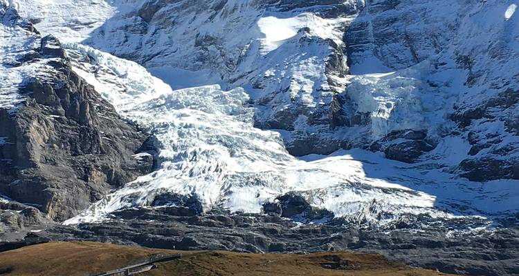 Primer plano de un glaciar escarpado y picos cubiertos de nieve con primer término rocoso.