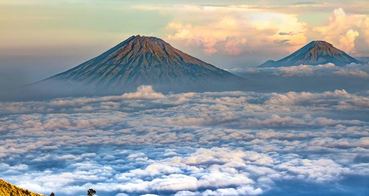 Dos picos volcánicos que se elevan sobre una gruesa capa de nubes durante la luz colorida del amanecer.
