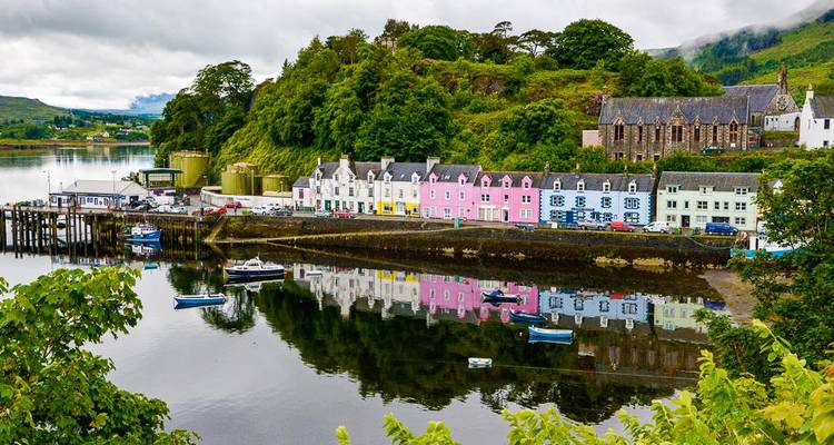 Die farbenfrohen Hafenhäuser von Portree spiegeln sich perfekt im ruhigen Hafenwasser wider, das von üppigen Bäumen umrahmt wird.