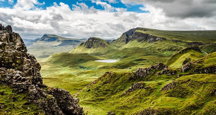 Weitläufiges grünes Tal und zerklüftete Grate des Quiraing unter dramatischen Wolken auf der Isle of Skye.