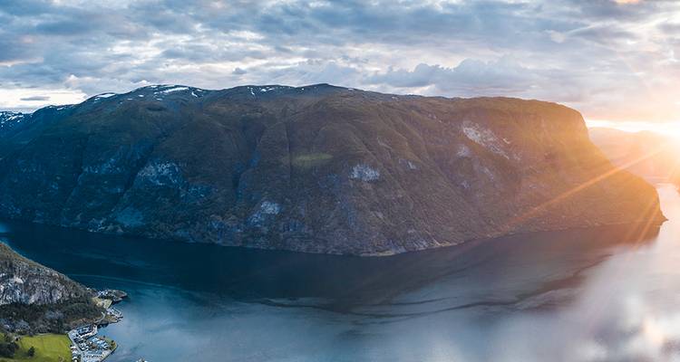 Luchtfoto van een steil fjord bij zonsopgang met gouden lensflare die de rotswand raakt.