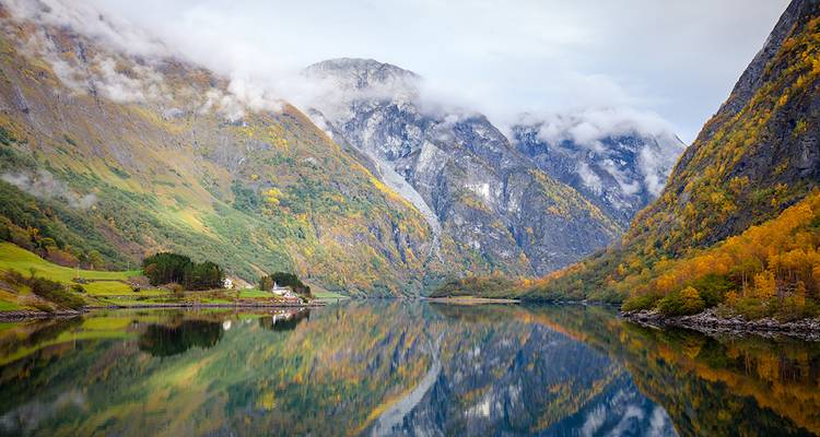 Spiegelgladde fjord weerspiegelt steile herfstgekleurde hellingen en mistige toppen.