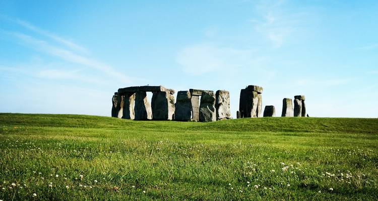 Vue panoramique lointaine de Stonehenge se dressant dans un champ herbeux ouvert sous un ciel bleu.