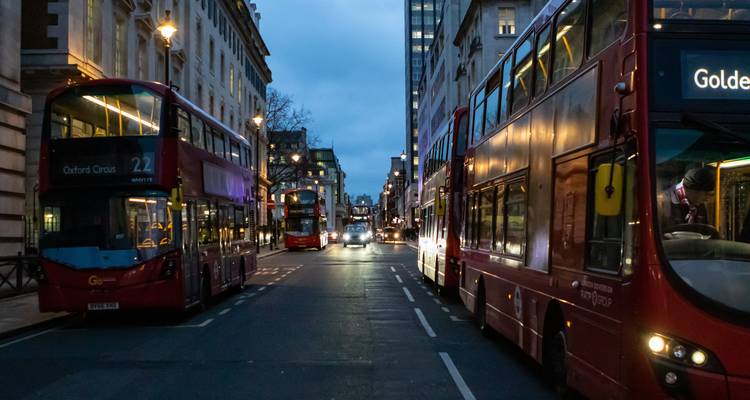 Scène de rue en soirée à Londres avec des autobus à deux étages iconiques de couleur rouge alignés le long de la route.