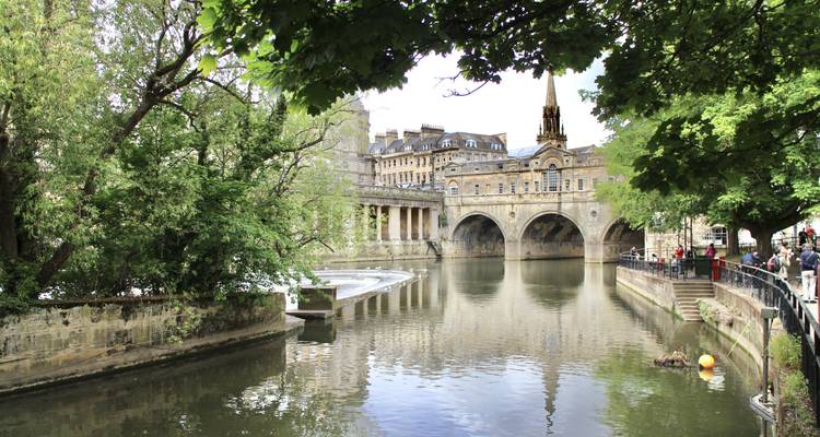 Vue sereine du Pont Pulteney et de la rivière Avon encadrés par des arbres feuillus à Bath.