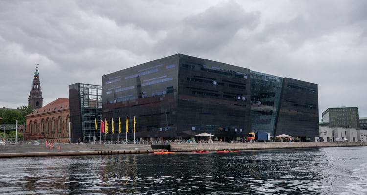 Facade lisse noire de la bibliothèque Black Diamond et du clocher historique adjacent reflétés dans le port avec des kayakistes.