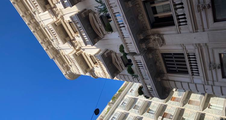 Elegante witte art-nouveau gevel met balkons en planten tegen een levendige blauwe lucht in Bari.