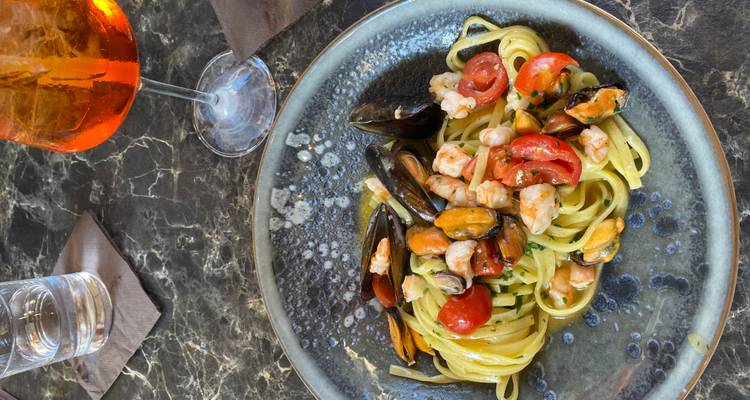 Zeevruchten linguine met mosselen, garnalen en cherry tomaten geserveerd op een keramisch bordje naast een Aperol spritz.