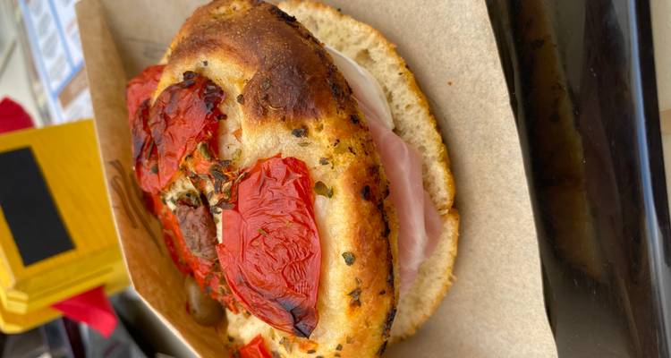 Close-up van een focaccia sandwich gevuld met ham en kaas, afgetopt met geroosterde tomaten.