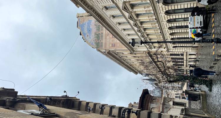 Smalle, regenachtige straat omzoomd met klassieke gebouwen en een muurschildering die over de daken uitkijkt