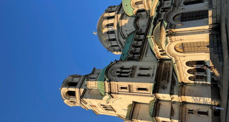 La masiva Catedral de Alexander Nevsky se eleva imponente capturada en la cálida luz del atardecer con algunos visitantes cerca de los escalones.
