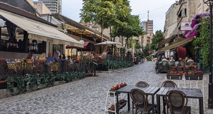 Encantadora calle empedrada en Skadarlija llena de cafés, flores y comensales disfrutando de mesas al aire libre.