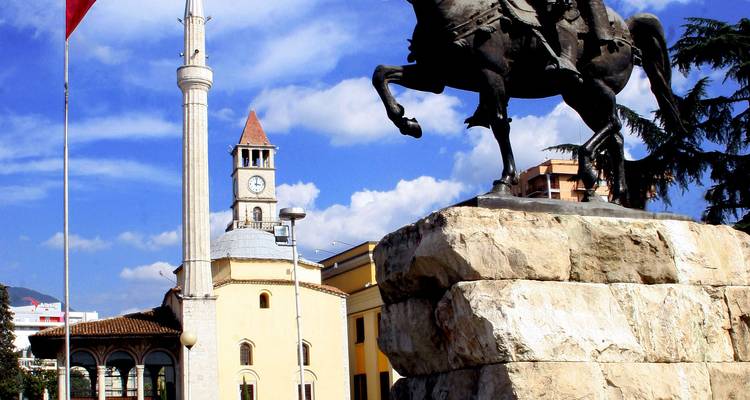 Ruiterstandbeeld van Skanderbeg met moskeeëminaretje en klokkentoren onder blauwe hemel