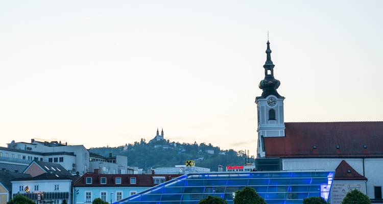 Kerkspits en bergbasiliek als silhouet tegen een bleek avondhemel in Linz