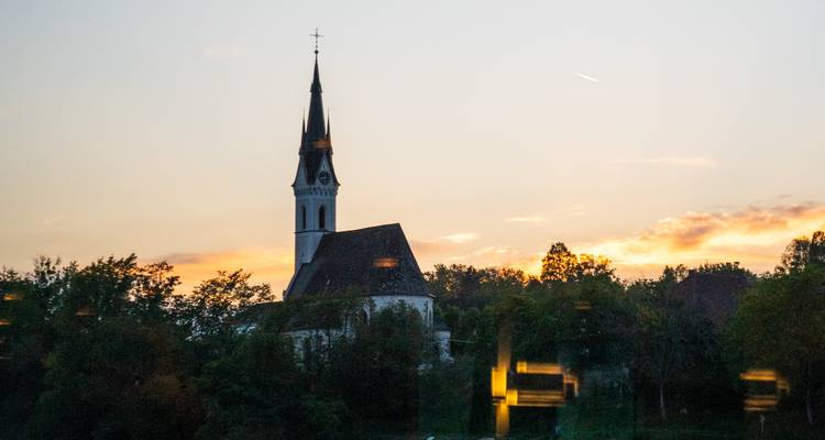Silhouette einer ländlichen Kirchturmspitze in der Dämmerung mit orangefarbenen Wolken im Hintergrund