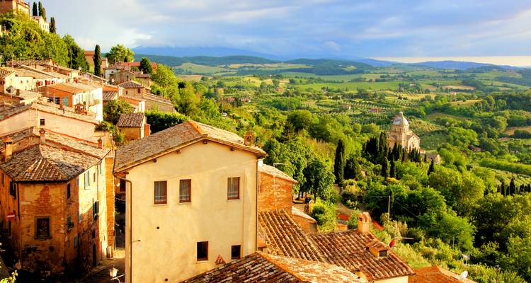 Zonnig stenen dorpje en glooiende groene Toscaanse landschap met een kerkkoepel in de verte