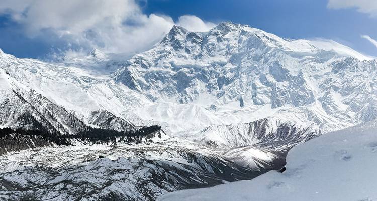 Vasta maciza cubierta de nieve del Nanga Parbat se alza sobre valles tallados por glaciares bajo cielos azules y cristalinos.
