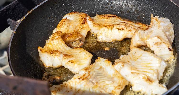 Filets de poisson frais grésillant dans le beurre dans une poêle noire à frire en plein air