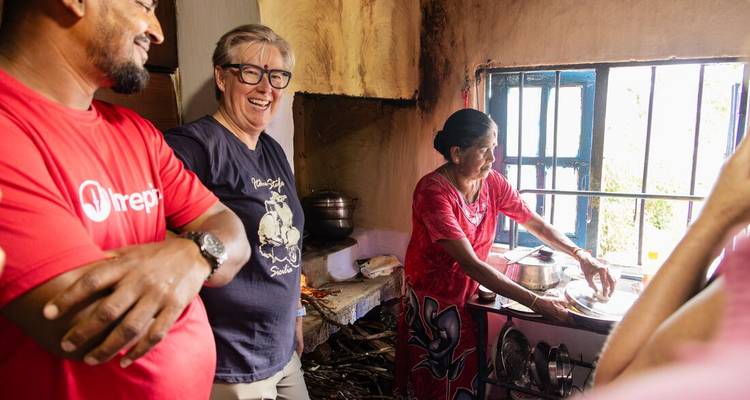 Reizigers lachen met een lokale vrouw die aan het koken is op een open fornuis in een dorpskeuken.