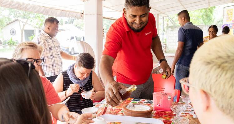 Lokale gastheer in rood shirt giet saus voor gasten die rond een feestelijke eettafel zitten.
