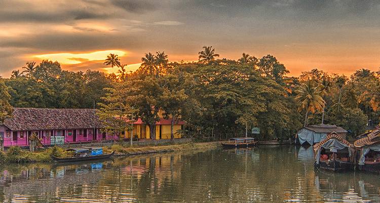Coucher de soleil doré sur les maisons colorées au bord du canal et les péniches dans les backwaters du Kerala.