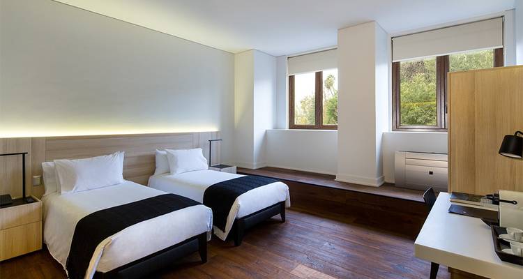 Modernes Hotelzimmer mit Doppelbetten und großen Fenstern sowie Holzböden.