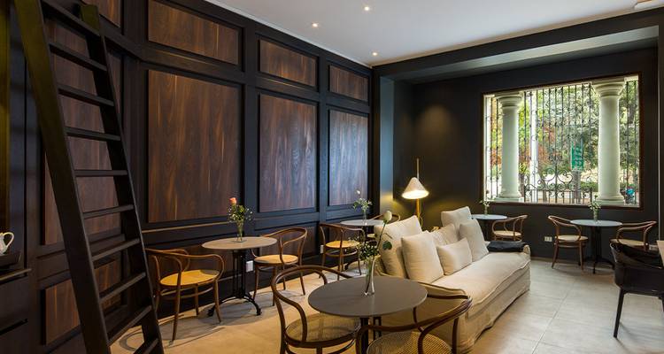Elegante Café-Lounge mit dunklen Holzpaneelen, kleinen Tischen und einem cremefarbenen Sofa.