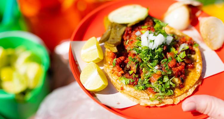 Taco de rue vibrant garni de coriandre, de salsa et de quartiers de citron vert sur une assiette rouge.