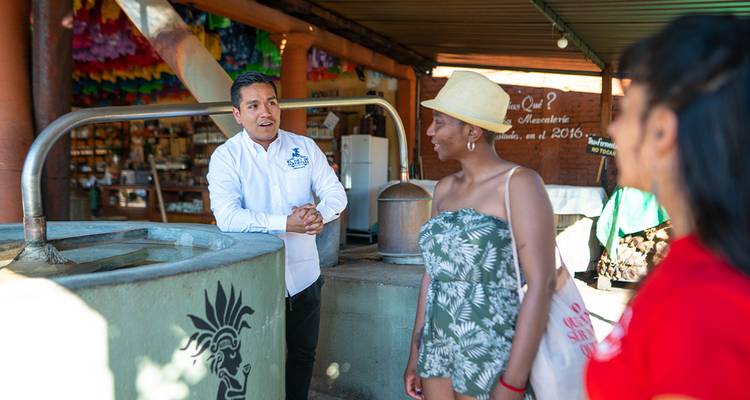 Un guide local explique la production de mezcal à deux voyageurs dans une distillerie.