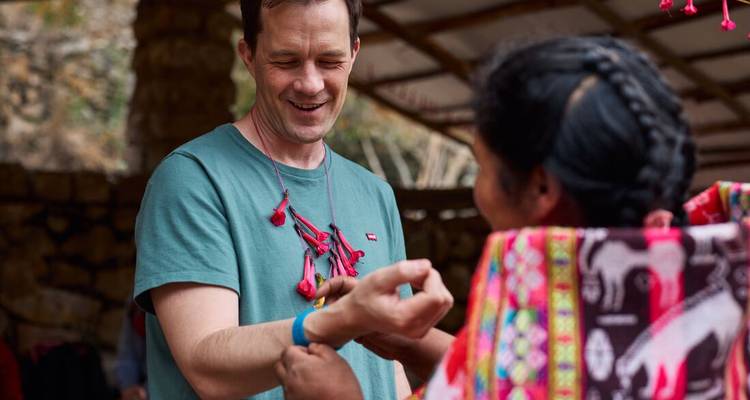 Een lokale ambachtsman bindt een geweven armband om de pols van een bezoeker in Peru.
