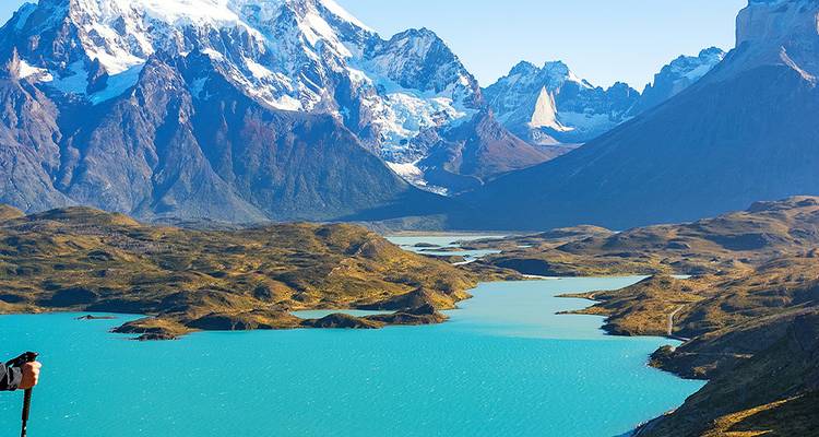 Enorm turkoois meer omgeven door ruwe granieten torens en met sneeuw bedekte toppen van Torres del Paine met een eenzame trekker die van het uitzicht geniet.
