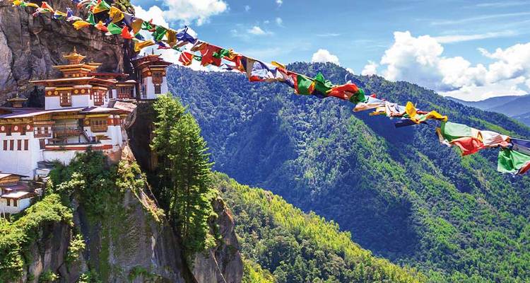 Le Monastère du Nid du Tigre s'accroche à une paroi rocheuse vertigineuse avec des drapeaux de prière colorés s'étendant sur une vallée himalayenne d'un vert profond.