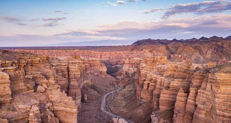Luchtfoto van de dramatische okergele rotsformaties van de Charyn Canyon die zich naar de horizon slingeren bij zonsondergang.