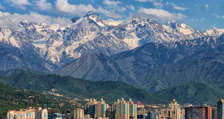 Stadsgezicht van Almaty met op de achtergrond de dramatische, ruige Tian Shan-bergen met verse sneeuw op de toppen onder een heldere hemel.