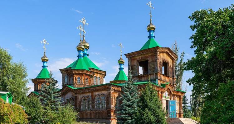 Houten Heilige Drie-eenheidskerk in Karakol met levendige groene daken en gouden orthodoxe kruizen tegen een blauwe lucht.