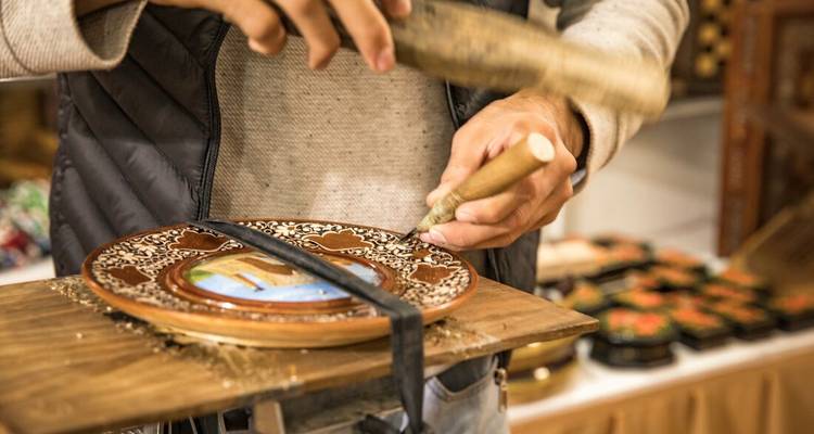 Un artisan cisèle une assiette en céramique ornée sur un petit tour dans un atelier ouzbek.