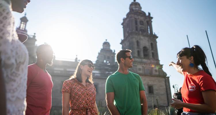 Guide gestures toward Mexico City's cathedral as sun flares behind the historic tower