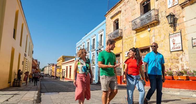 Travellers stroll a colorful colonial street lined with yellow and blue buildings under clear skies