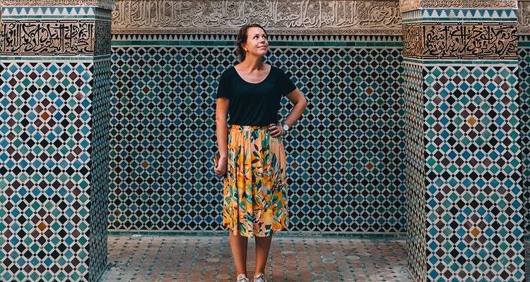 Reiziger staat voor prachtig betegelde muren en ingeweven Arabische kalligrafie in een Marokkaanse madrasa