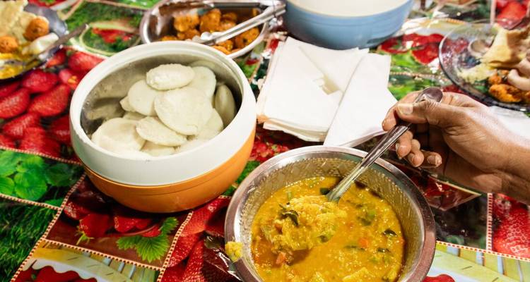 A close-up of a Sri Lankan meal featuring steamed idli cakes, lentil curry and chutneys on a colourful tablecloth.
