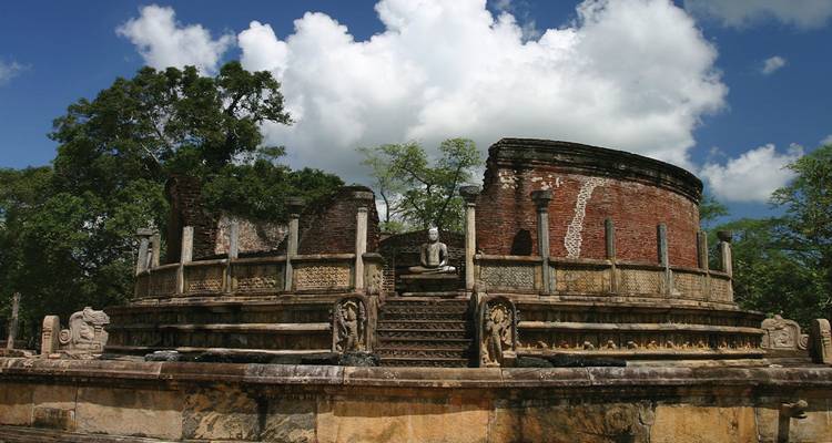 Ancient circular brick shrine with stone Buddha statues and carved guard stones set amid tropical trees.